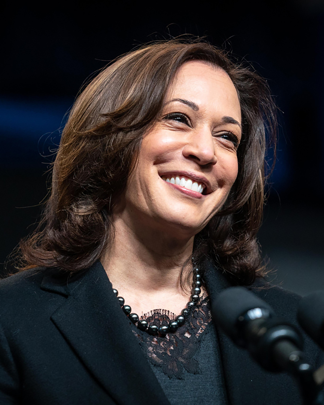 Kamala Harris, a light-skinned black woman wearing a dark suit, smiling